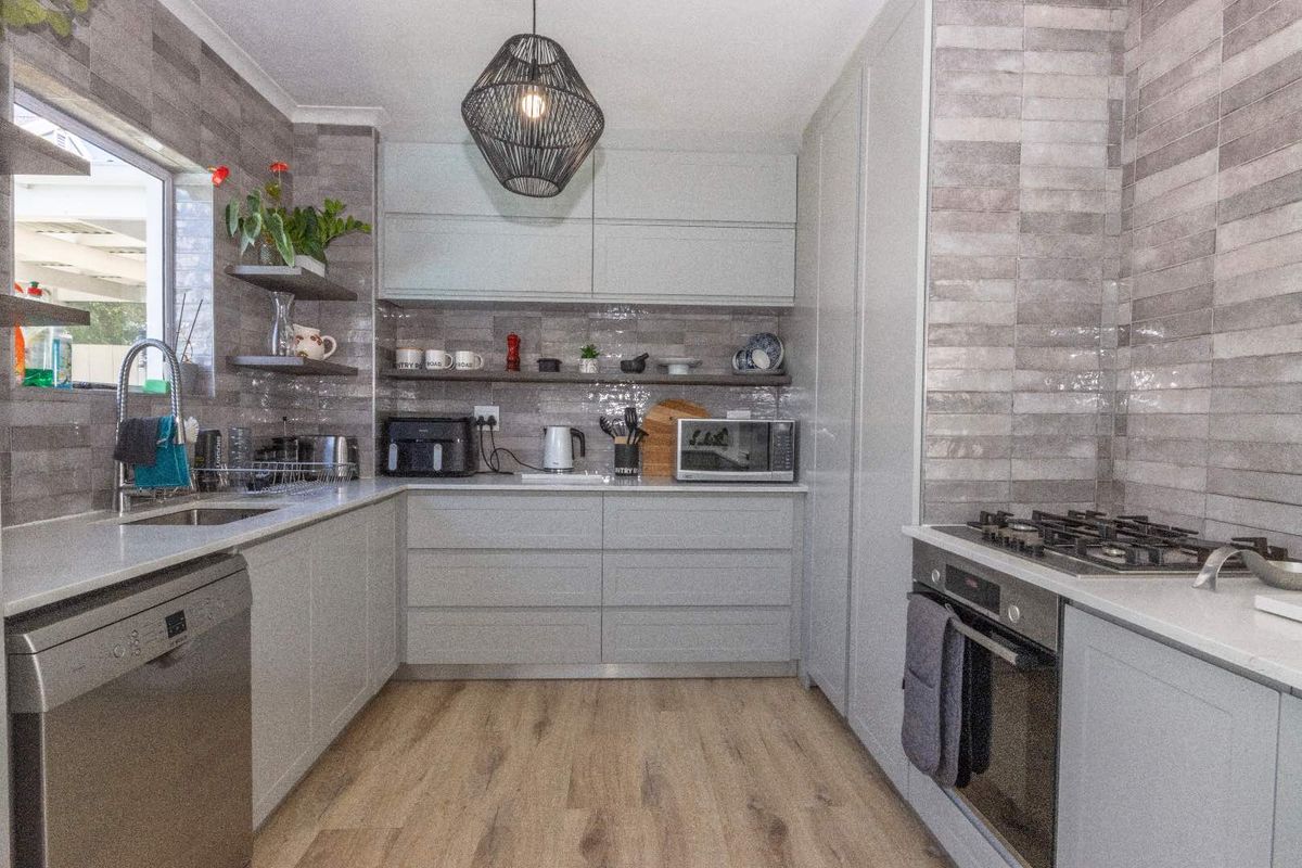 Modern kitchen featuring light grey cabinetry, stone countertops, gas hob, built-in oven, and stylish tiled splashback with wood-look laminate flooring.