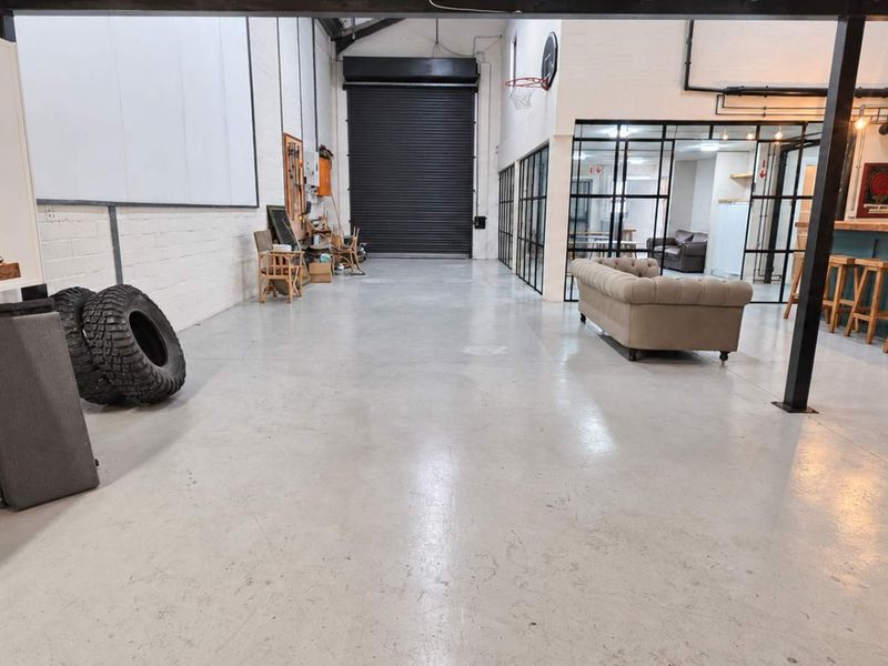 Spacious industrial open-plan area featuring polished concrete floors, exposed steel structural elements, a built-in bar, and large roller shutter access.