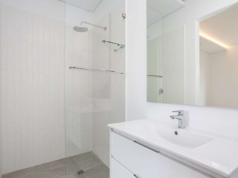 A modern, clean-lined bathroom featuring a walk-in shower with a glass screen, a sleek vanity with a basin, and a large wall-mounted mirror.