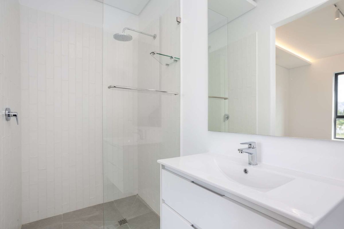 A modern, clean-lined bathroom featuring a walk-in shower with a glass screen, a sleek vanity with a basin, and a large wall-mounted mirror.