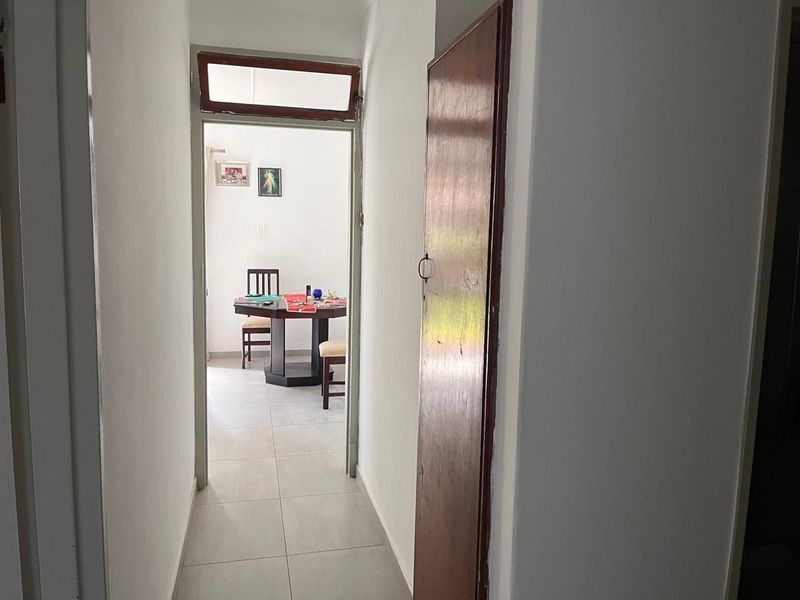 A narrow interior hallway featuring tiled flooring and a wooden door with a transom window, leading into an adjacent living space.