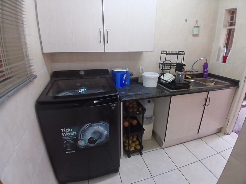 A functional laundry area featuring built-in cabinetry, a granite countertop with a stainless steel sink, and tiled finishes.