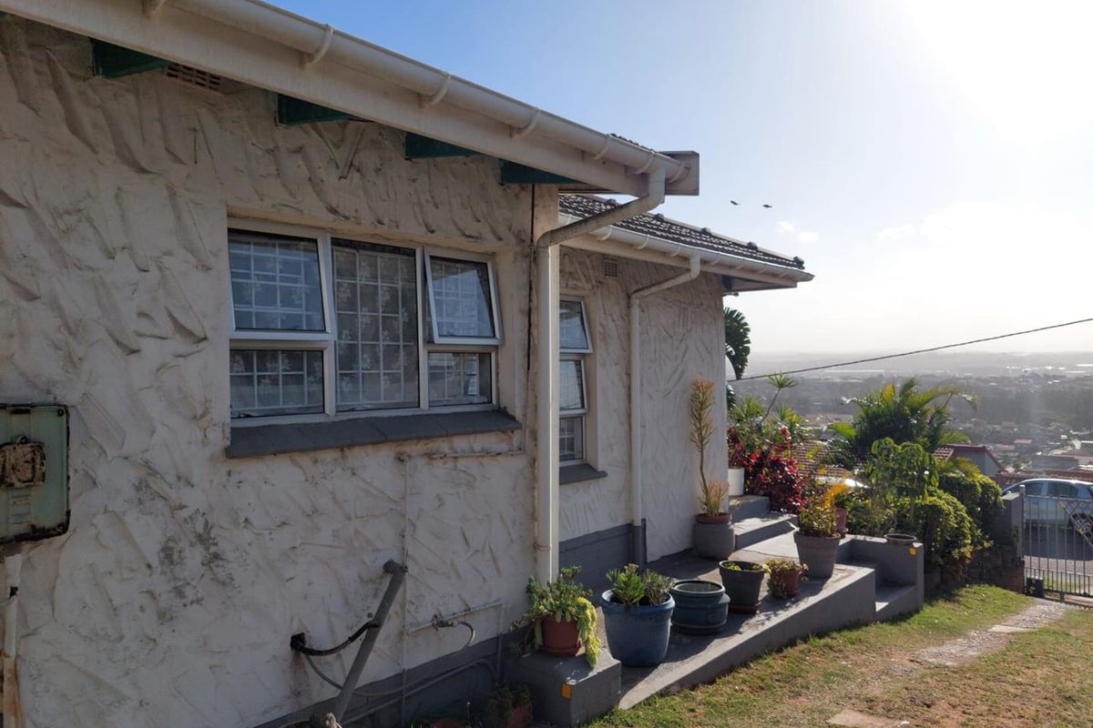 Rear exterior view of the house featuring textured stucco walls, aluminium window frames, and concrete steps leading to the garden area.