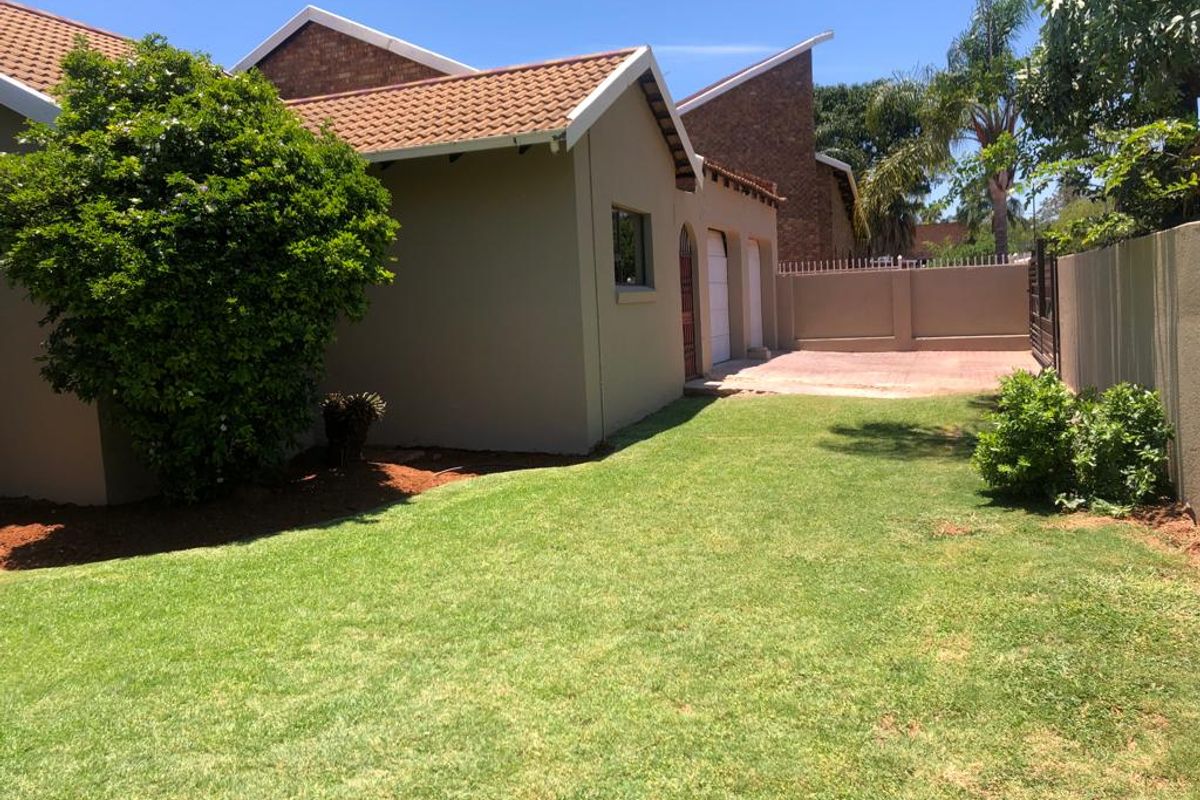 A view of the rear garden featuring a well-maintained lawn, paved driveway area, and brick perimeter walling.