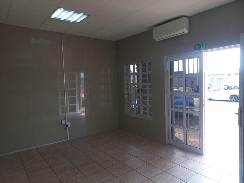 A vacant office space featuring tiled flooring, a suspended ceiling with recessed lighting, and a wall-mounted air conditioning unit with direct exterior access.