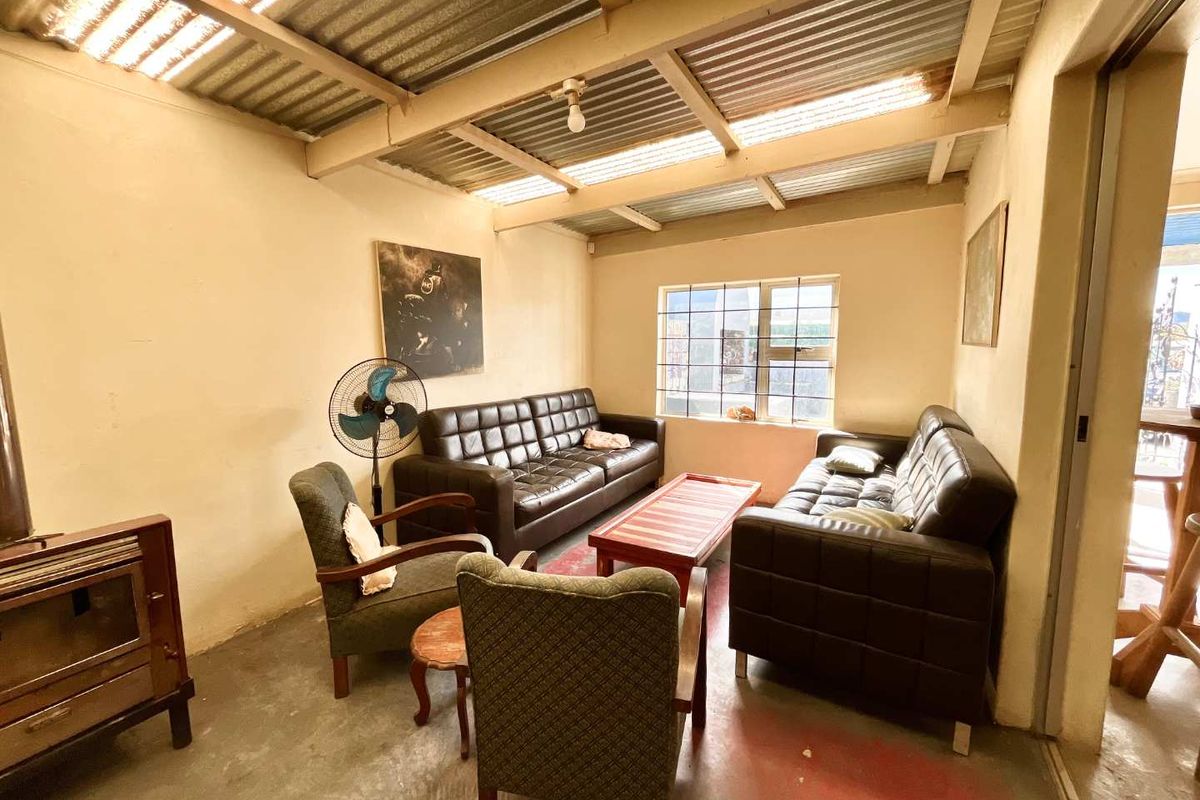 A rustic living area featuring exposed timber rafters, a corrugated iron roof, concrete flooring, and a built-in wood-burning stove.