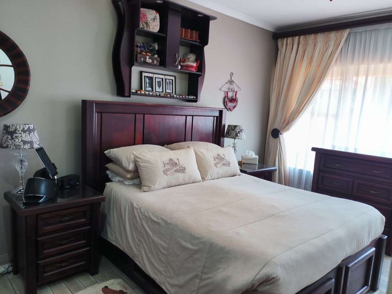 A cozy bedroom featuring neutral wall tones, built-in wall shelving, and large window treatments, providing a comfortable and functional sleeping space.