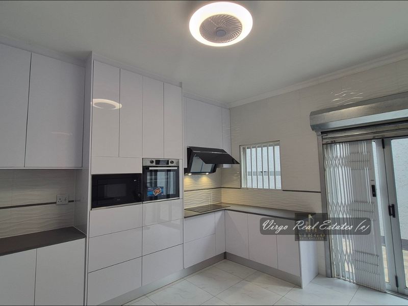 Modern kitchen featuring high-gloss white cabinetry, integrated appliances, tiled flooring, and direct access to an outdoor area through a sliding door with security gate.