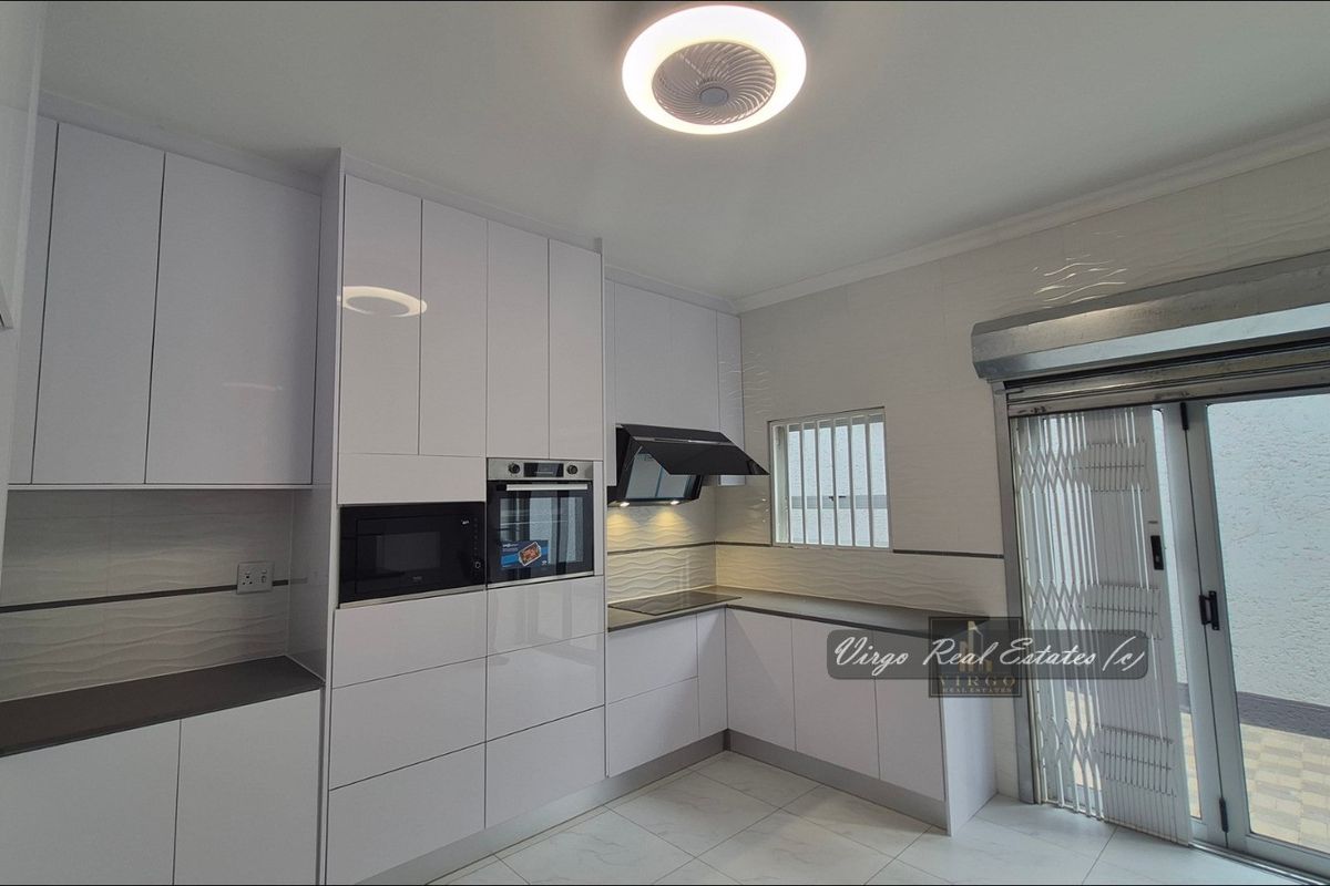 Modern kitchen featuring high-gloss white cabinetry, integrated appliances, tiled flooring, and direct access to an outdoor area through a sliding door with security gate.