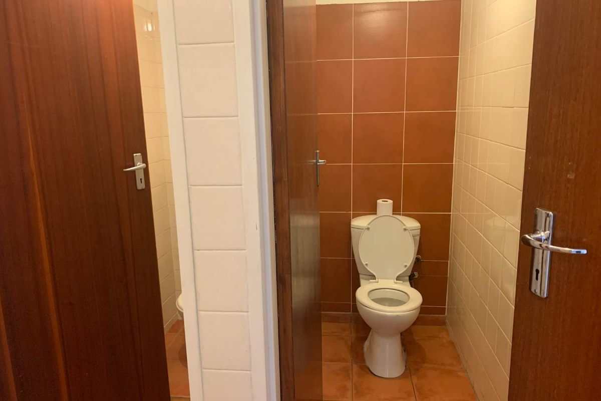 A functional office restroom featuring a standard toilet suite with dated terracotta-style wall and floor tiling.