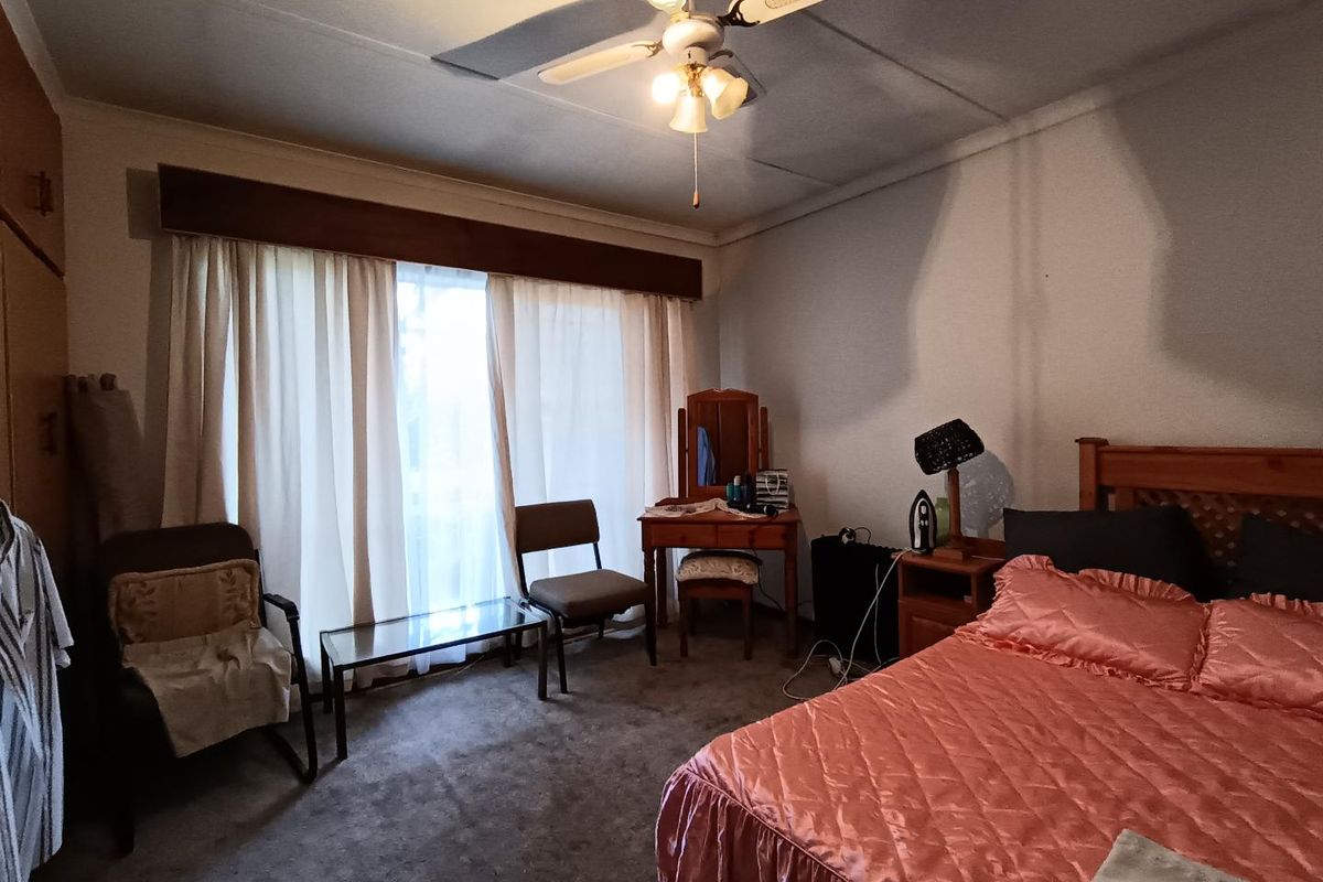 A spacious bedroom featuring built-in cabinetry, a ceiling fan, and large windows with curtain pelmets, offering a functional and traditional layout.