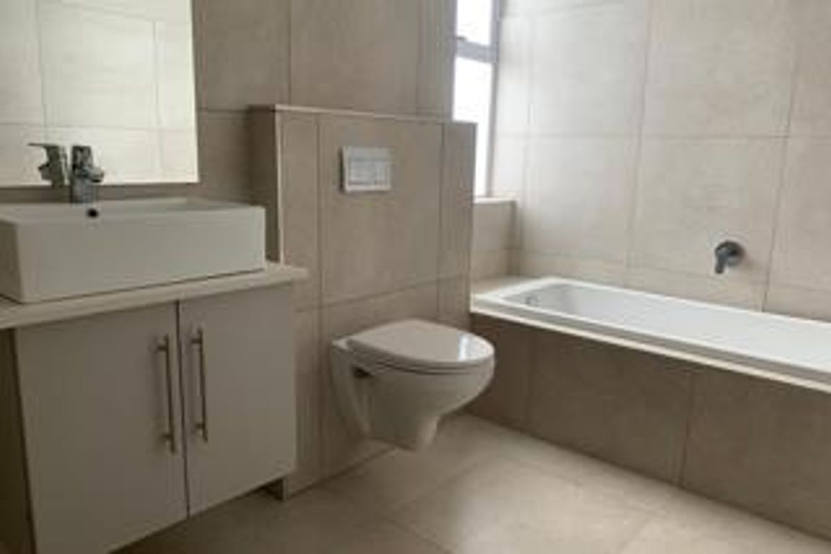 Modern bathroom featuring a wall-mounted toilet, built-in bathtub, and a vanity cabinet with a vessel sink, finished with neutral floor-to-ceiling tiles.