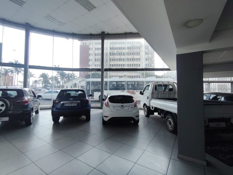 Spacious retail showroom featuring extensive floor-to-ceiling glass windows, tiled flooring, and modern structural columns, providing excellent visibility and natural light.