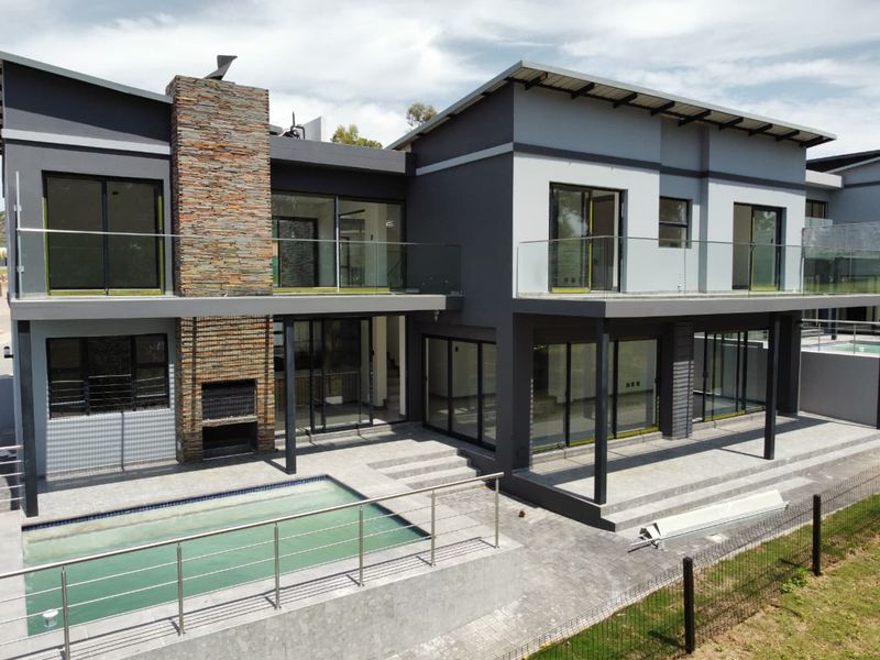 Modern double-story rear elevation featuring a stone-clad fireplace, swimming pool, expansive covered patio, and upper-level balconies with glass balustrades.