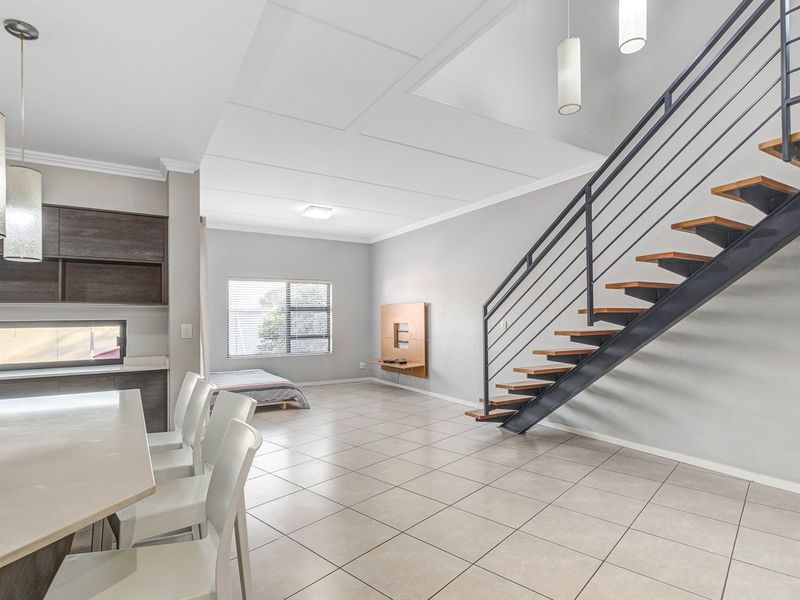 Spacious open-plan living area featuring tiled floors, a modern staircase with metal railings, and integrated kitchen cabinetry.