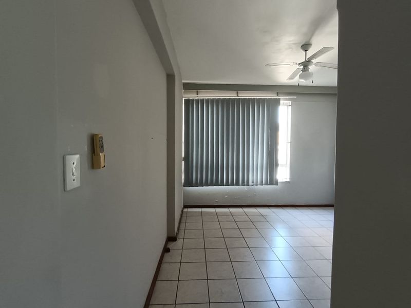 An empty living area featuring tiled flooring, a ceiling fan, and vertical blinds, showing signs of wear on the walls.
