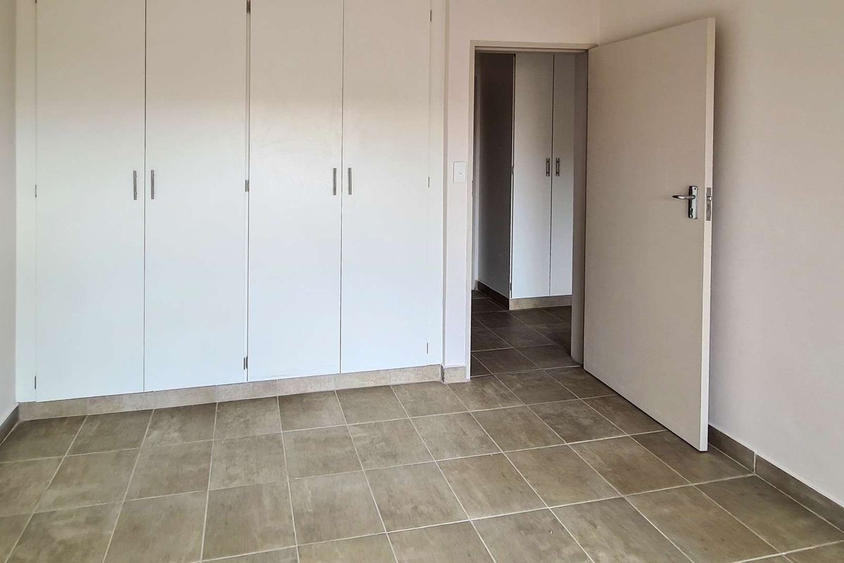 An empty bedroom featuring neutral tiled flooring and extensive built-in cupboard storage, leading into a hallway with additional storage.
