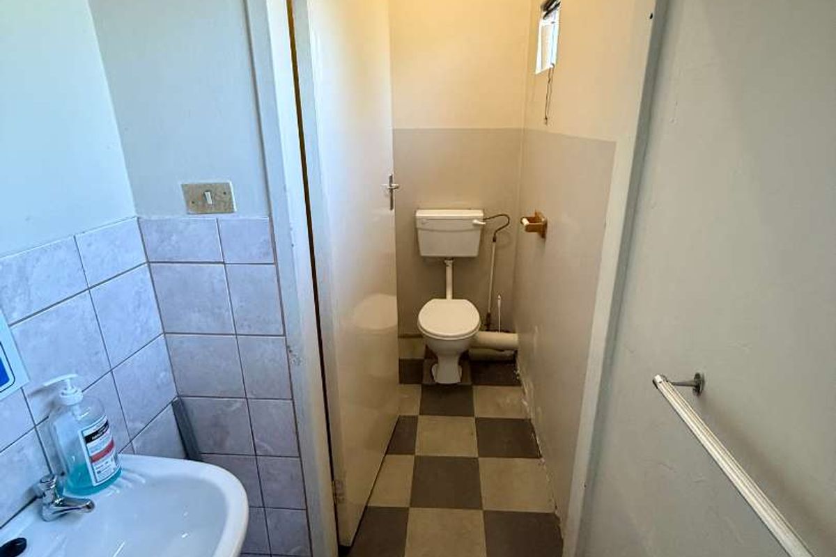 A functional bathroom featuring a pedestal washbasin and a separate toilet area with tiled flooring and wall finishes, requiring cosmetic updates.