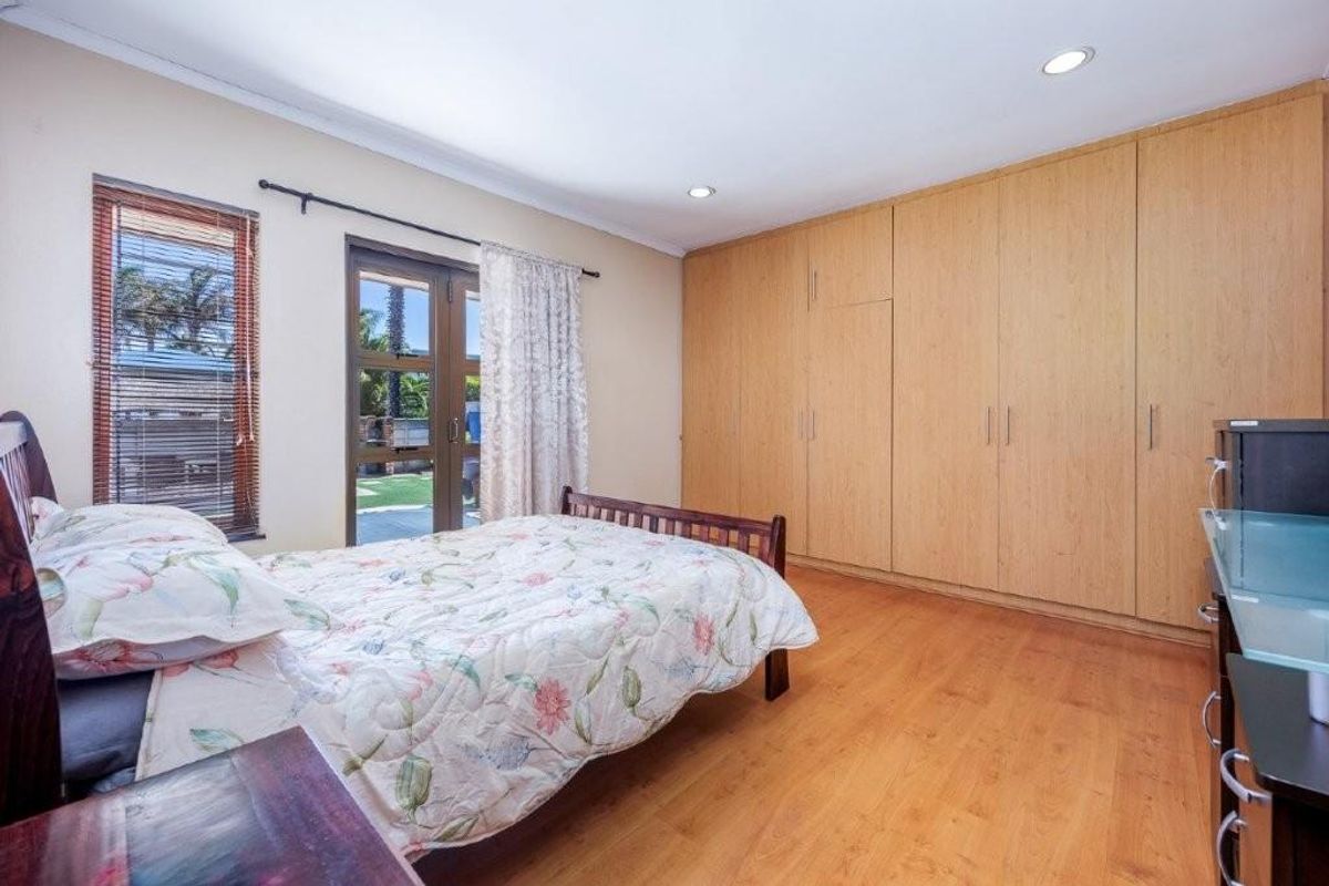 A bedroom featuring built-in wooden cupboards, laminate flooring, recessed ceiling lighting, and glass sliding doors providing access to the outdoor area.