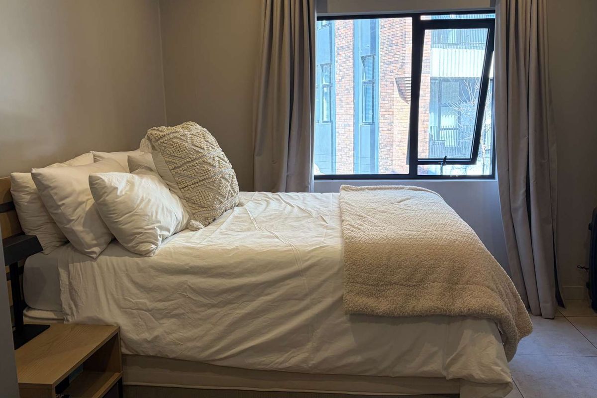 A well-maintained bedroom featuring neutral wall tones, tiled flooring, and a large window with modern aluminium frames.