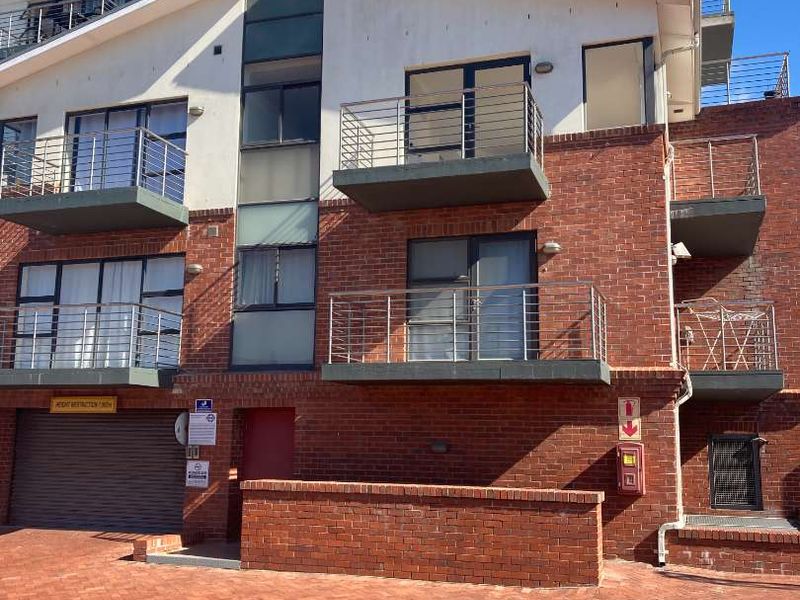 Front elevation of a multi-story apartment building featuring face-brick construction, multiple balconies with stainless steel railings, and a paved driveway entrance.