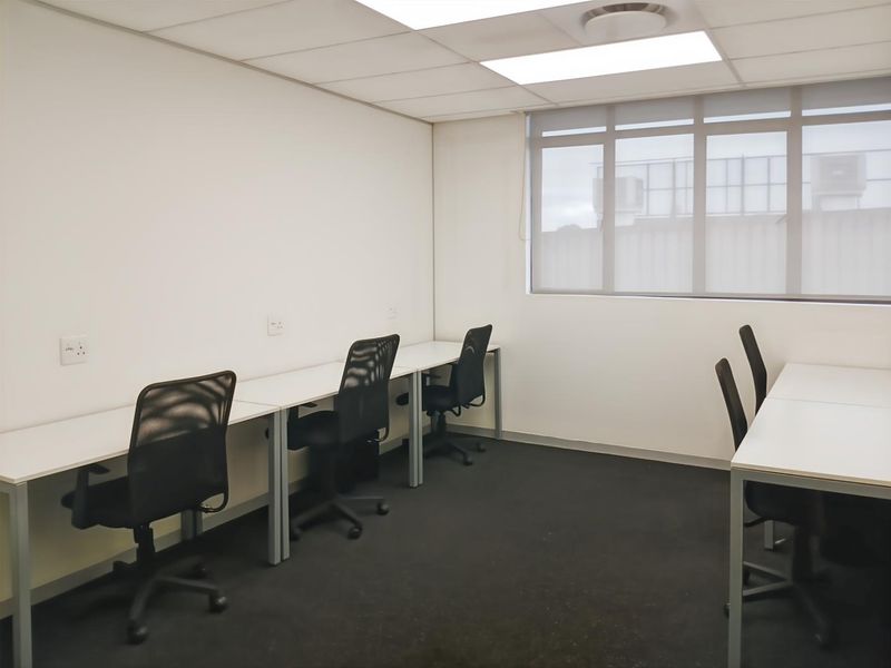 A functional office space featuring a suspended ceiling, recessed lighting, and large windows with roller blinds, providing a clean and professional work environment.