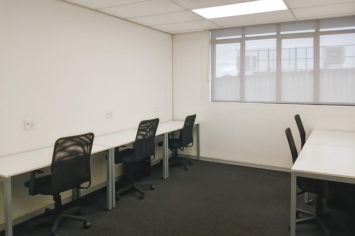 A functional office space featuring a suspended ceiling, recessed lighting, and large windows with roller blinds, providing a clean and professional work environment.