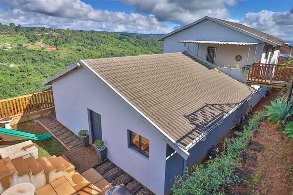 Rear view of the property featuring a tiled roof, paved patio area, and timber balustrades, set against a scenic hillside landscape.
