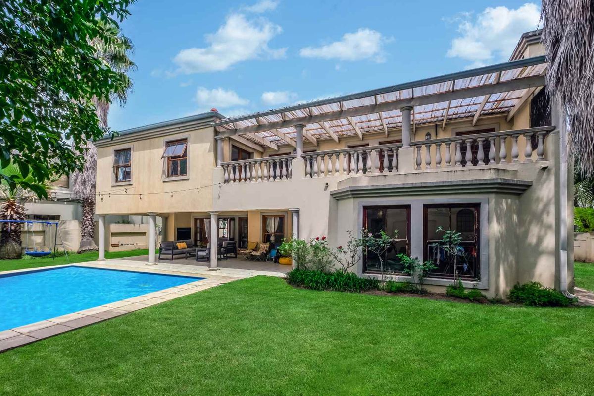Rear view of a two-story house featuring a swimming pool, a covered ground-floor patio, and an upper-level balcony with a balustrade.
