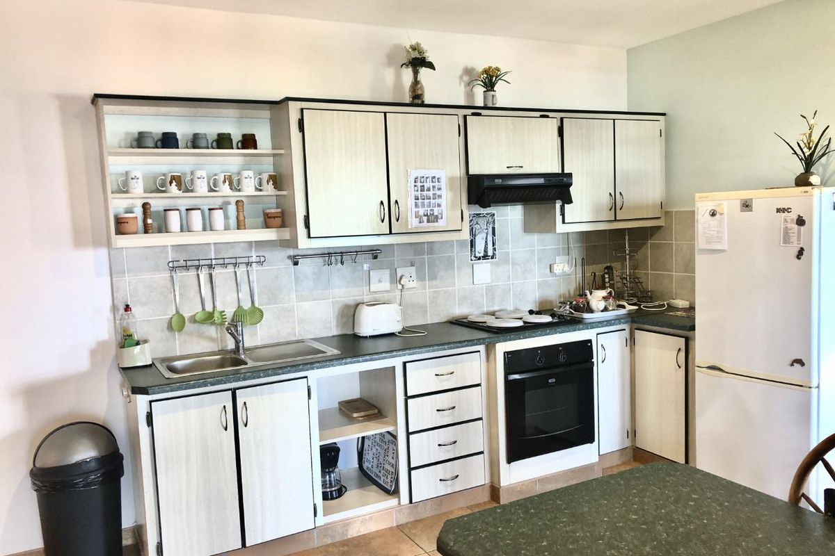 A functional kitchen featuring light-toned cabinetry, tiled backsplash, built-in oven, extractor fan, and a double stainless steel sink.