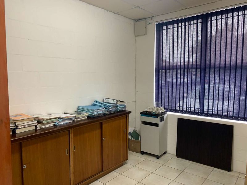 A functional office space featuring built-in wooden storage cabinetry, tiled flooring, and vertical window blinds, providing a practical workspace environment.