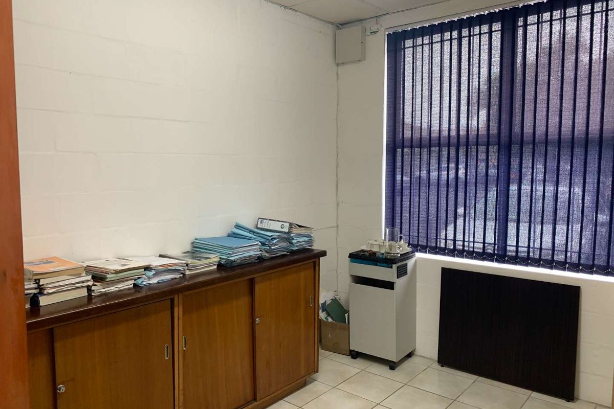 A functional office space featuring built-in wooden storage cabinetry, tiled flooring, and vertical window blinds, providing a practical workspace environment.