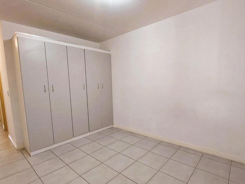 A clean, empty bedroom featuring neutral tiled flooring and ample built-in cupboard storage space.
