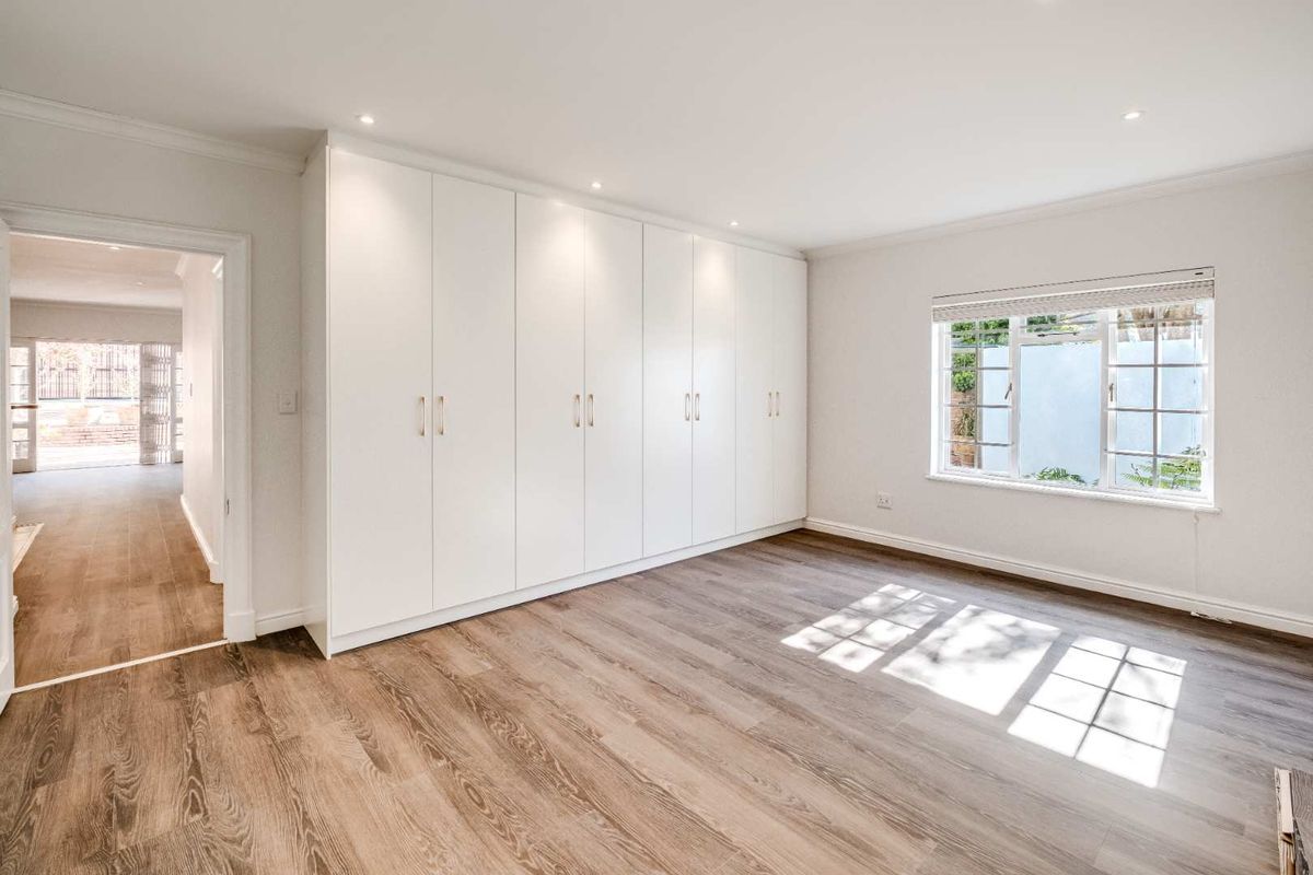 A bright, empty bedroom featuring modern laminate flooring, extensive built-in floor-to-ceiling cupboards, and recessed downlighting.