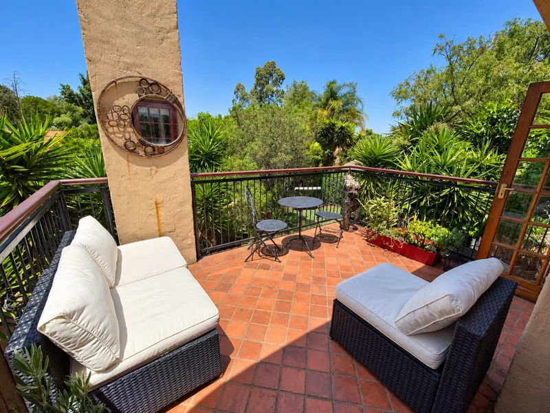 A sunny balcony featuring terracotta tile flooring, a wrought iron railing, and a stucco pillar, offering a pleasant outdoor space.