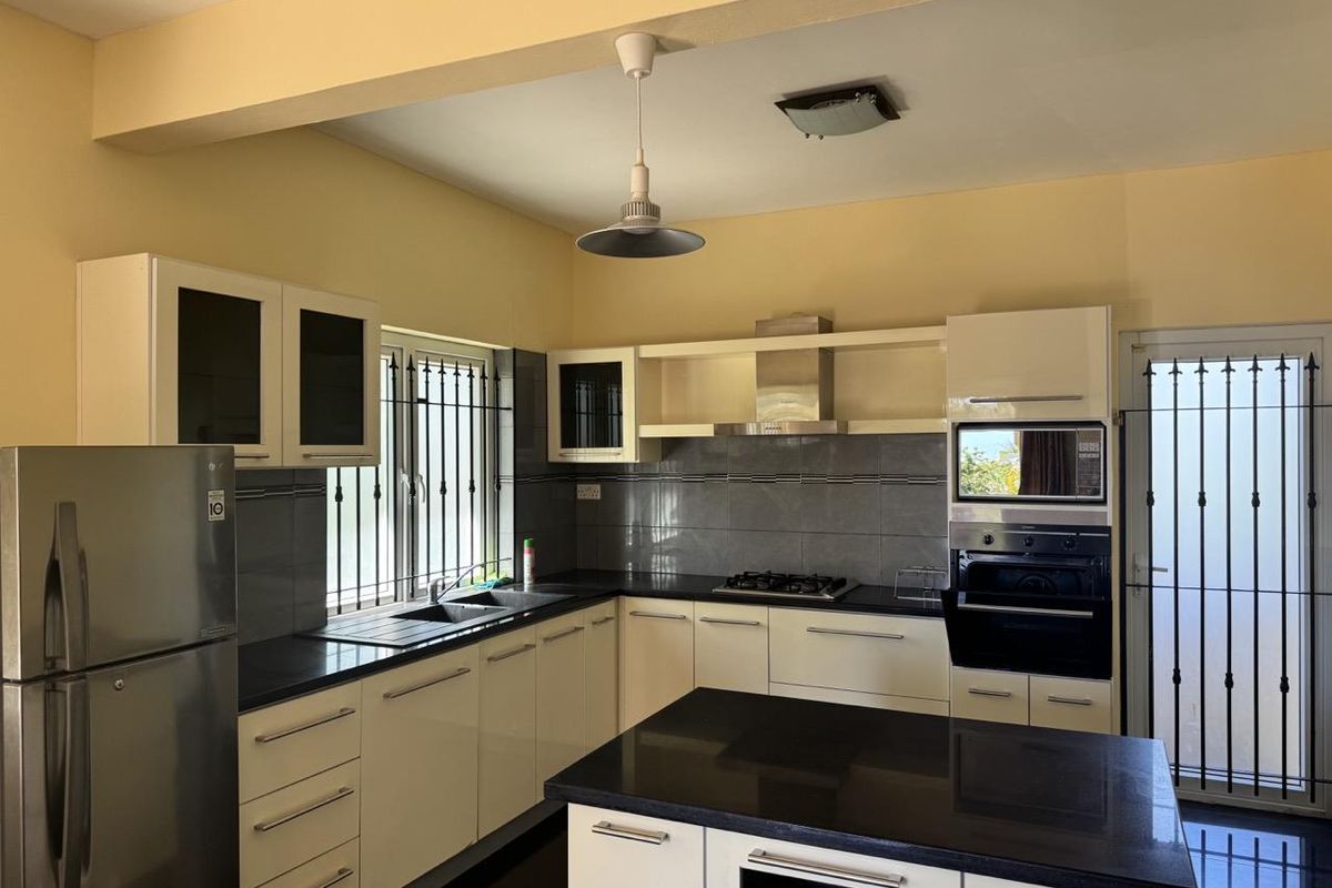 A functional kitchen featuring dark granite countertops, white cabinetry, a built-in oven, gas hob, extractor fan, and a central island.