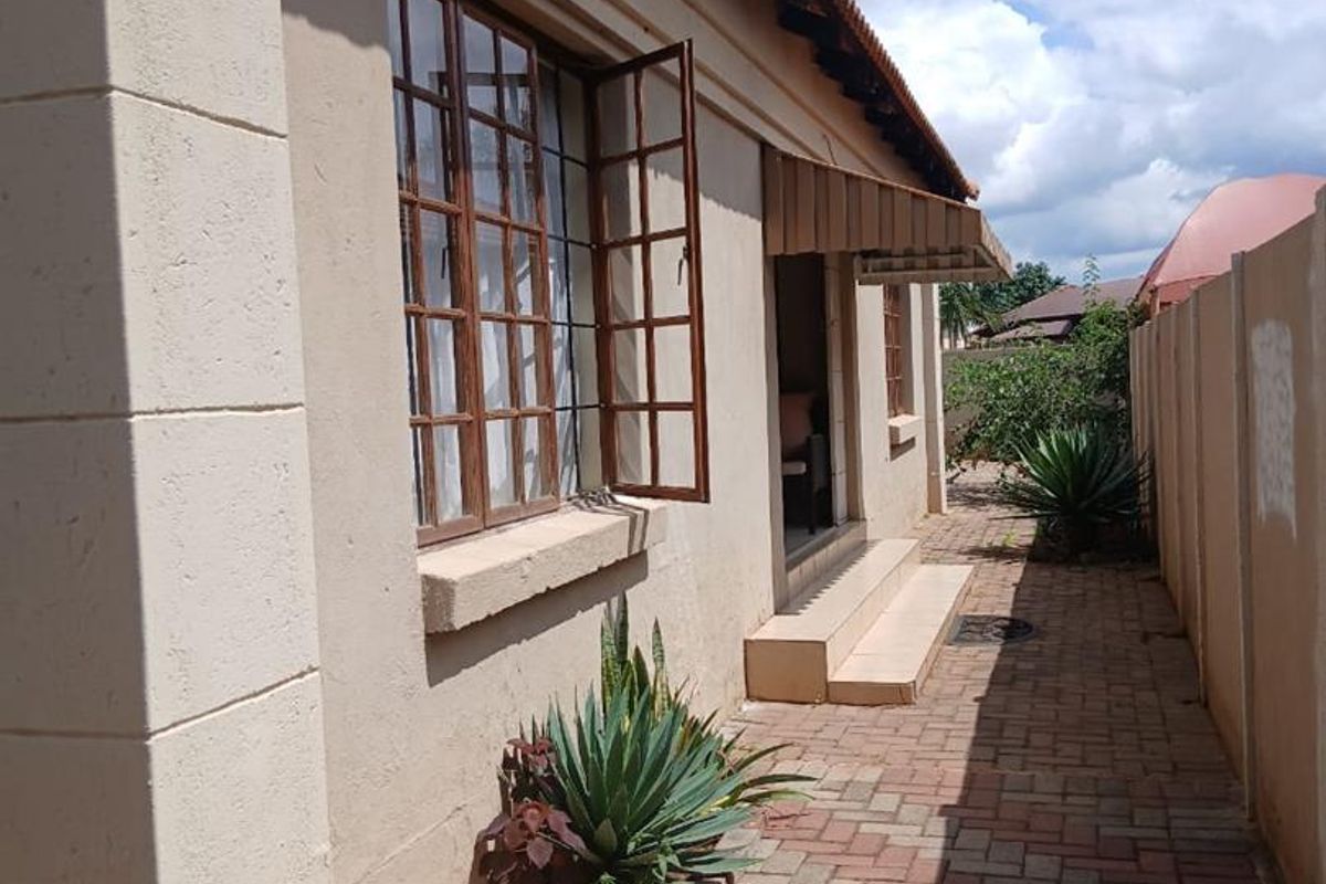 Side exterior view of the house featuring paved walkway, timber-framed windows, and a small covered entrance area.