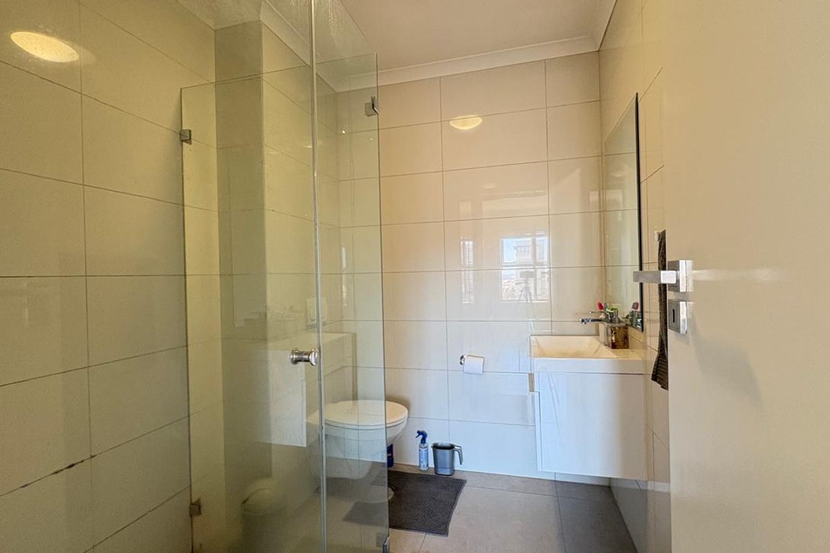 A compact bathroom featuring a glass-enclosed shower, wall-mounted vanity with basin, and tiled walls and flooring.