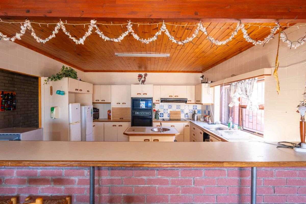 Spacious kitchen featuring a breakfast bar, built-in double oven, cooktop, and timber ceiling beams, offering a functional layout with significant potential for modern renovation.