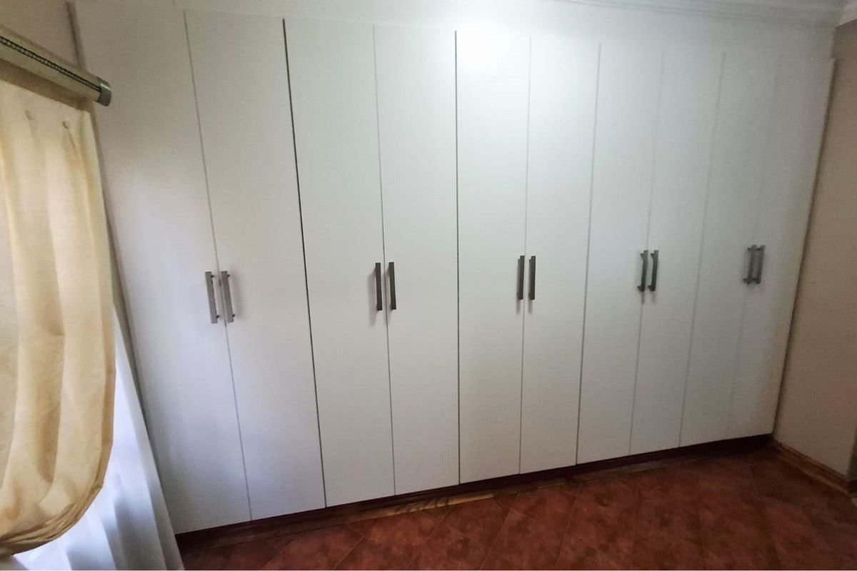 A bedroom featuring a wall of white built-in cupboards and tiled flooring.