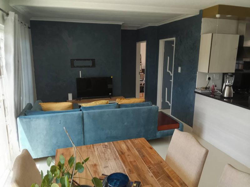 Open-plan living and dining area featuring a modern kitchen with dark cabinetry and granite countertops, flowing into a comfortable lounge space.
