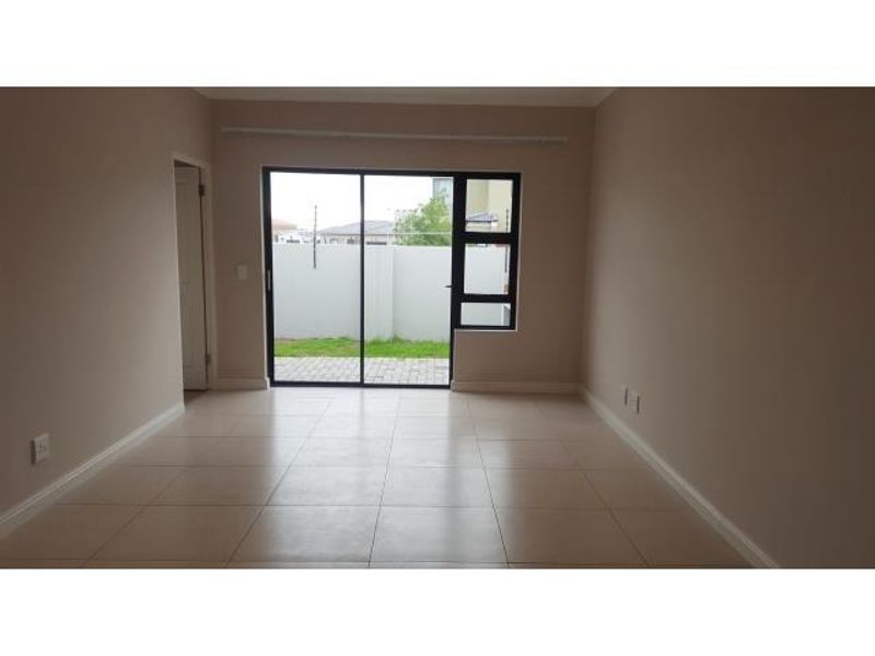 A bright, empty living room featuring neutral tiled flooring and a large sliding glass door providing access to the rear garden area.