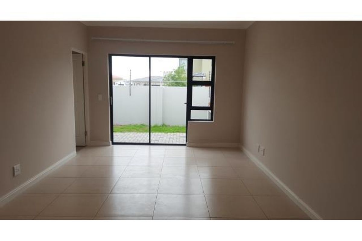 A bright, empty living room featuring neutral tiled flooring and a large sliding glass door providing access to the rear garden area.