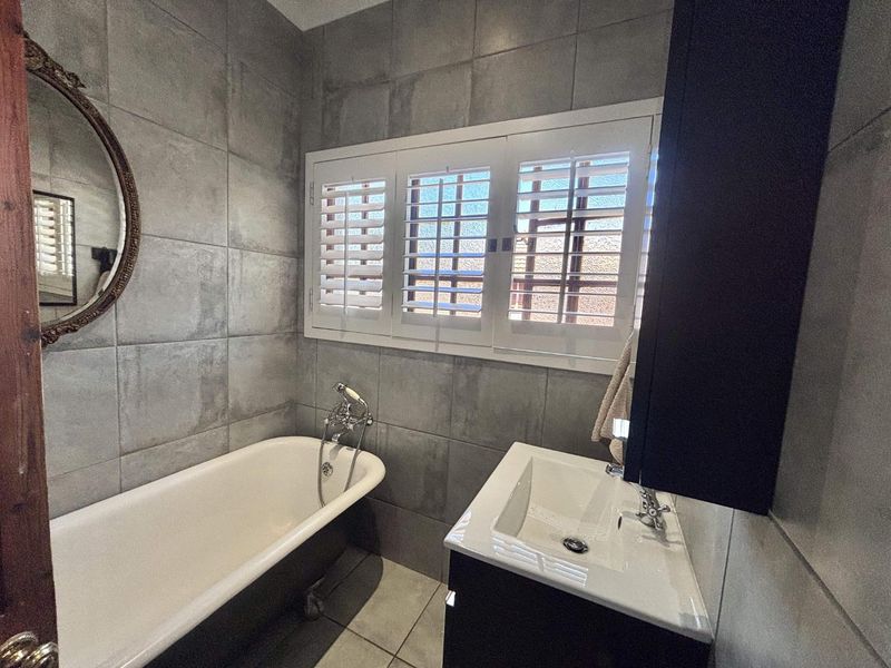 Modern bathroom featuring a freestanding bathtub, wall-mounted basin, and stylish grey tiled walls with plantation-style shutter blinds.