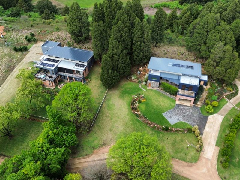 Aerial view of a residential property featuring two modern homes with solar panels, surrounded by lush green lawns and mature trees.