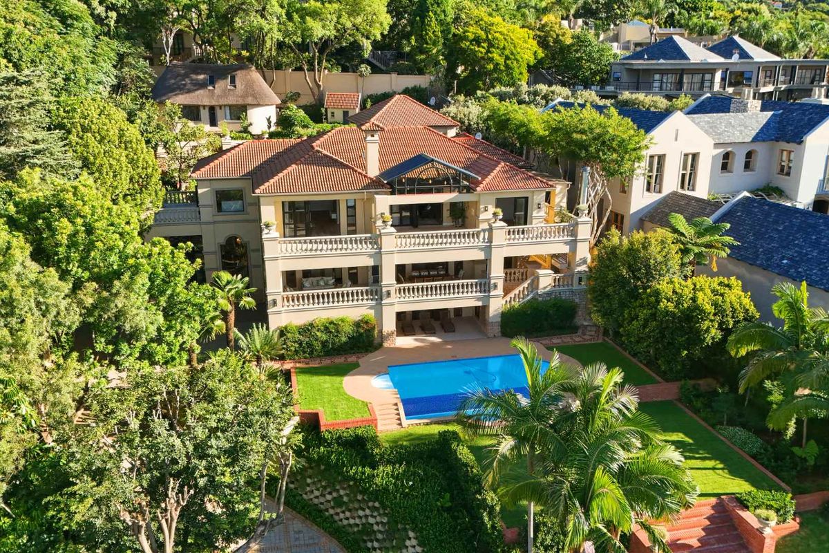 Aerial view of a multi-story luxury residence featuring a swimming pool, expansive tiered balconies, and lush landscaped gardens in a private estate setting.