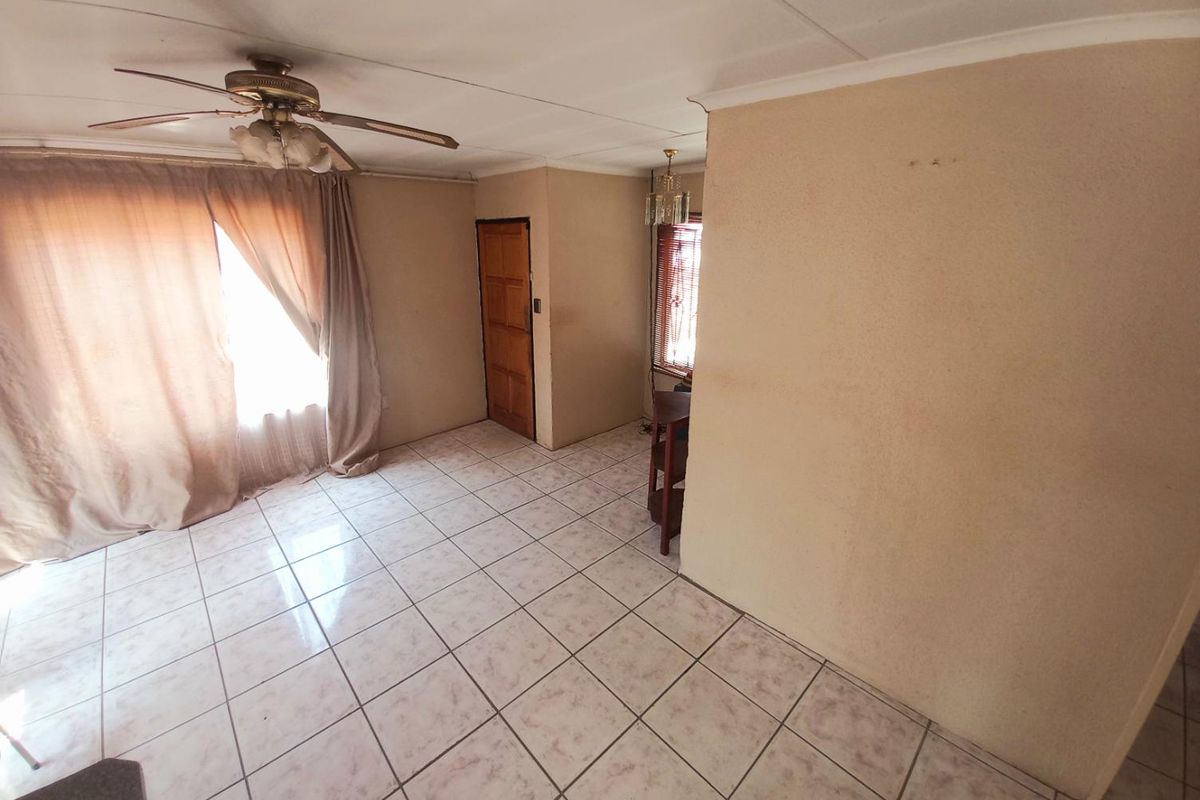 A living area featuring tiled flooring, a ceiling fan, and natural light through window treatments.