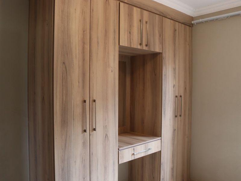 A bedroom featuring modern wood-grain built-in wardrobes with an integrated vanity station and crown molding detail.
