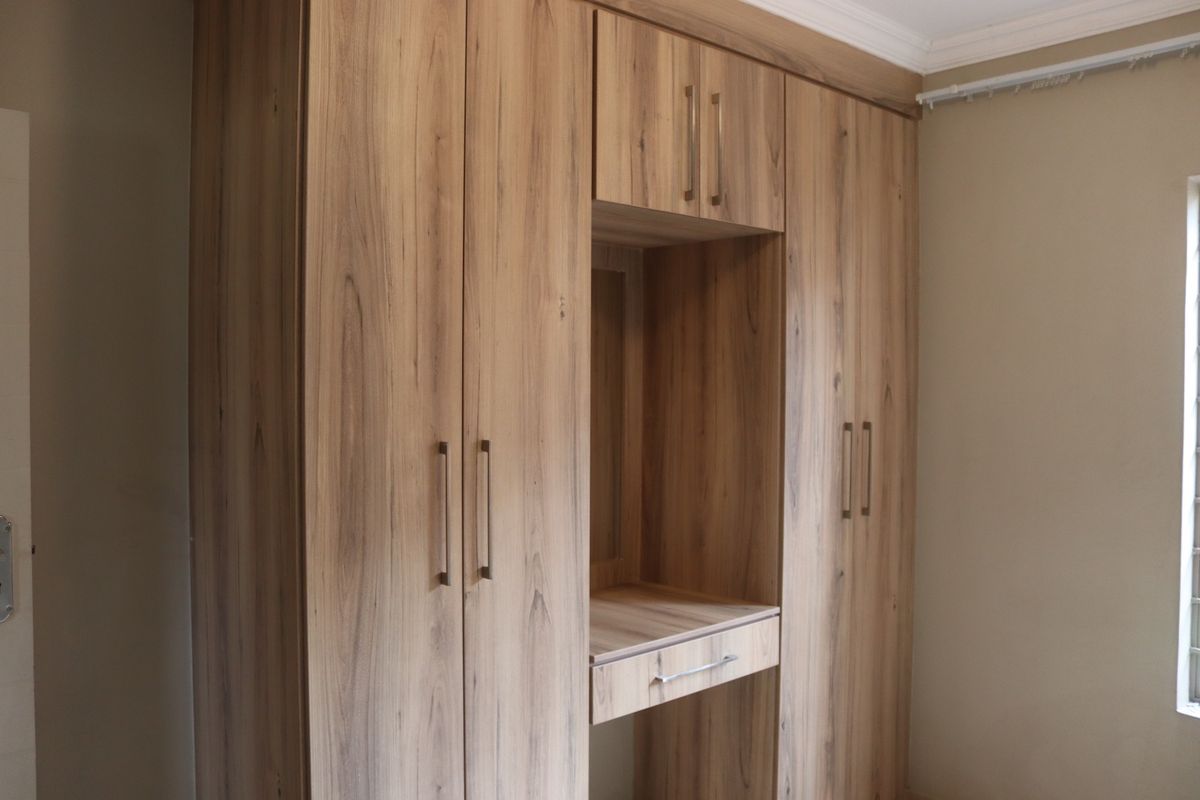 A bedroom featuring modern wood-grain built-in wardrobes with an integrated vanity station and crown molding detail.