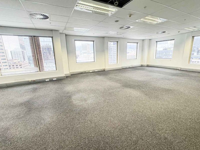 An open-plan office space featuring a suspended ceiling, recessed lighting, and large windows with city views, currently vacant and ready for customization.